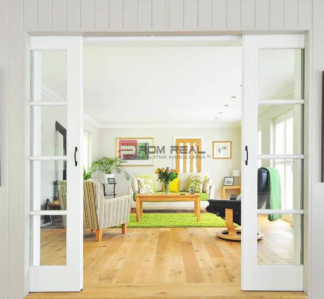 A bright living room with glass doors, wooden flooring, a sofa, and a table in a studio apartment.