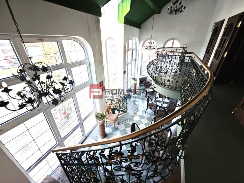 The interior features an elegant staircase and a balcony on Ľ. Podjavorinská Street, with oversized windows highlighting the historic building.