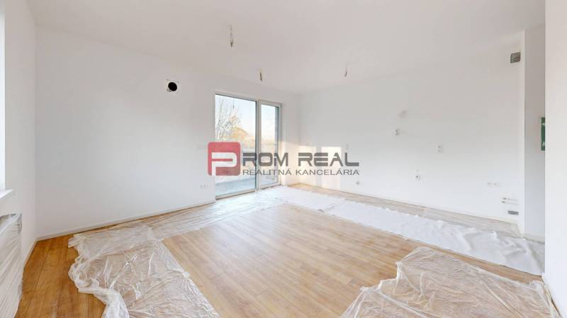 A bright room with large windows and wooden flooring in a 2-room apartment.