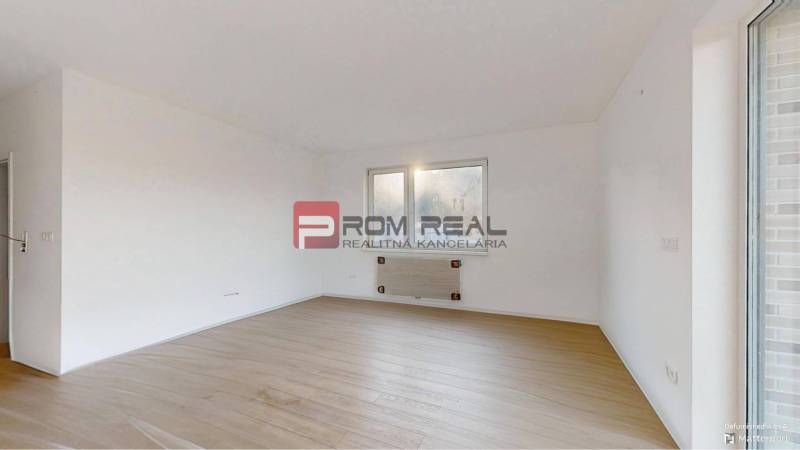 A room in a two-room apartment with white walls and wooden flooring.
