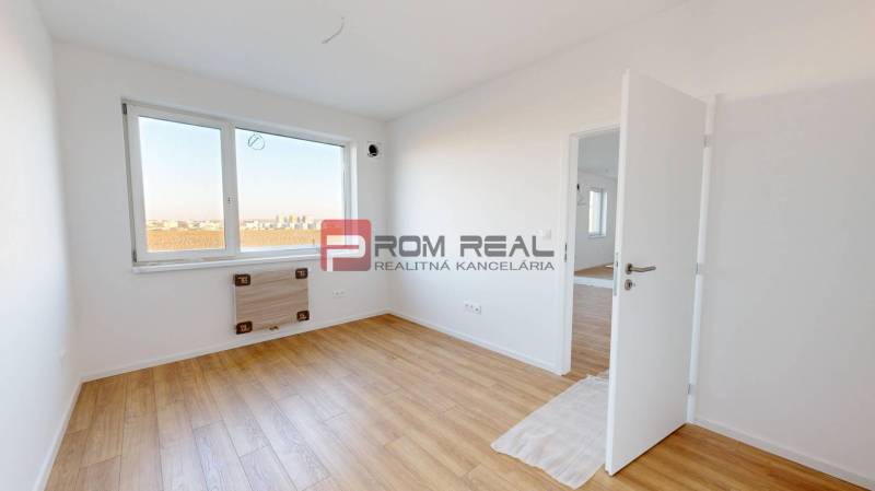 A bright room in a 2-room apartment with wooden flooring and a large window.