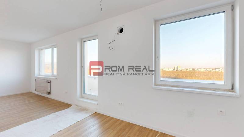 A bright room with wooden flooring and large windows in a 2-room apartment.