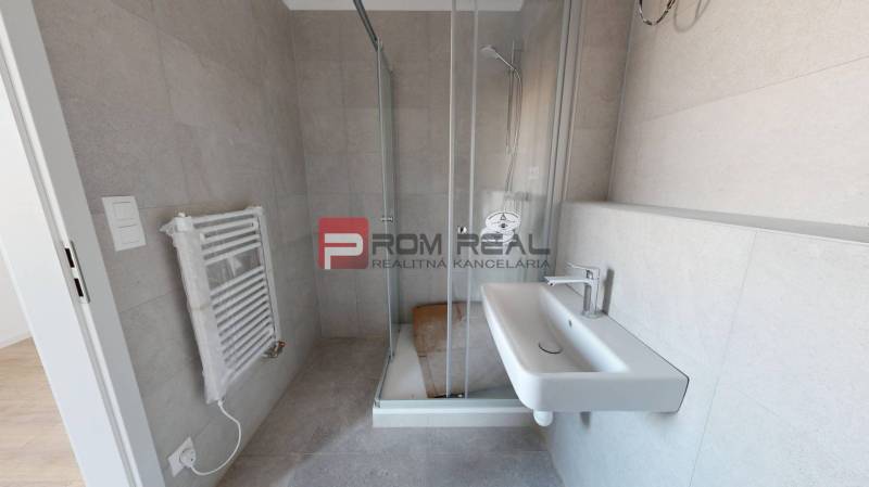 Bathroom in a 2-room apartment with a sink, shower corner, and ladder radiator.
