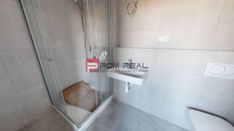 Bathroom in a 2-room apartment with a shower, sink, and light-colored tiles.