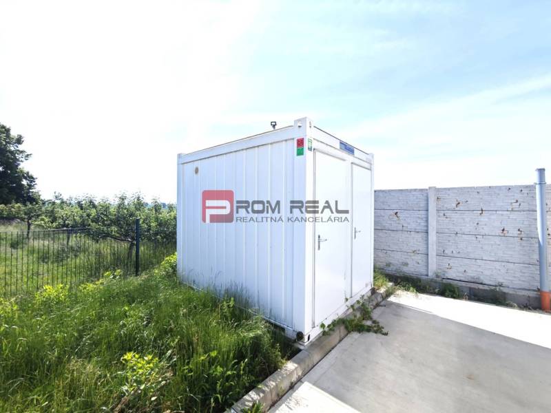 A white container next to the fence and concrete area on Šúrska Street in Modra.