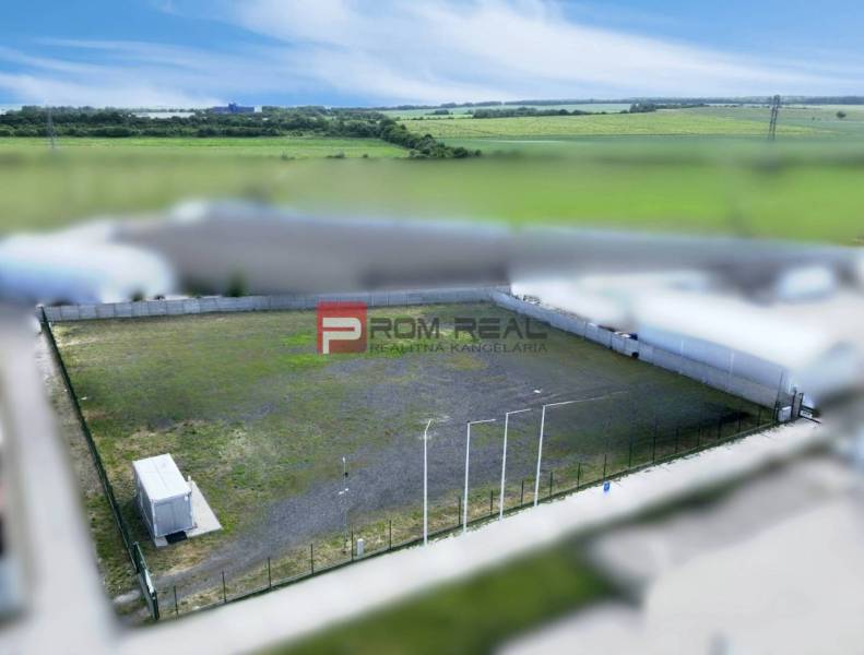 Production premises in Pezinok with a fenced outdoor area and a container, surrounded by fields.