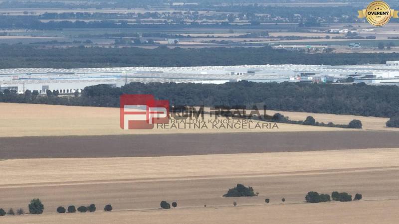 Countryside with agricultural land near Senecká Street, distant industrial buildings.