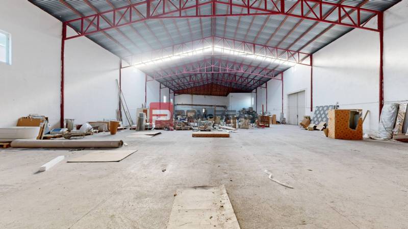 A spacious interior of a building with stored materials and an open ceiling with red beams.