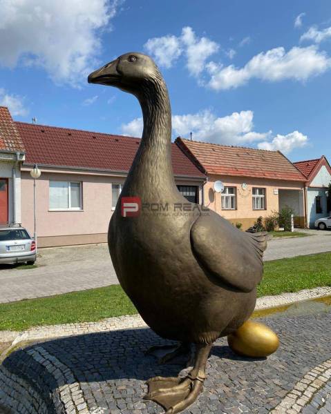 A statue of a goose with a gilded egg on Slovenský Grob street, with warehouses and halls in the background.