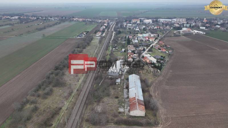 A railway track surrounded by fields and houses, on Partizánska Street, warehouses and halls are visible.