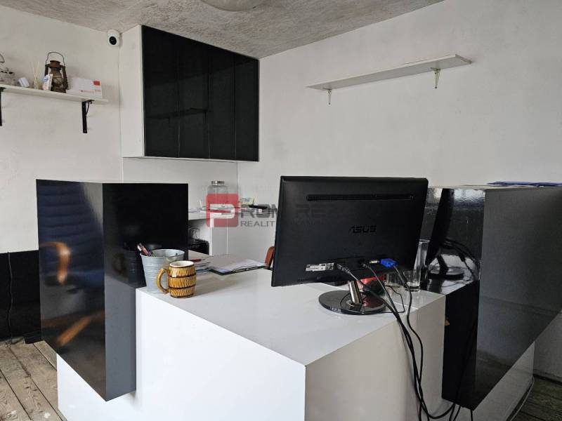 An office with a desk, monitor, and shelves, located on Partizánska Street near the warehouses.