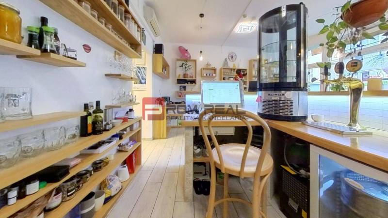 Interior of commercial premises with storage shelves, a wooden chair, and a counter with drinks.
