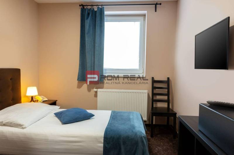 A room with a bed, a lamp, a television, and a window in an accommodation facility.