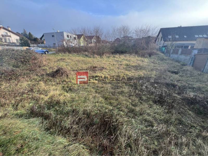 Stupava, Bazová: Residential land with overgrown grass and surrounding houses.
