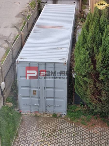 On Púchovská Street in Bratislava III, there is a shipping container next to greenery and a fence.
