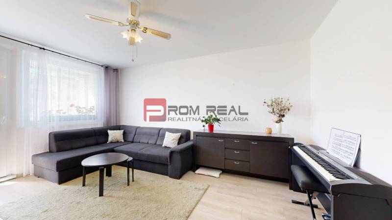 Living room in a three-room apartment with a dark sofa and a piano.