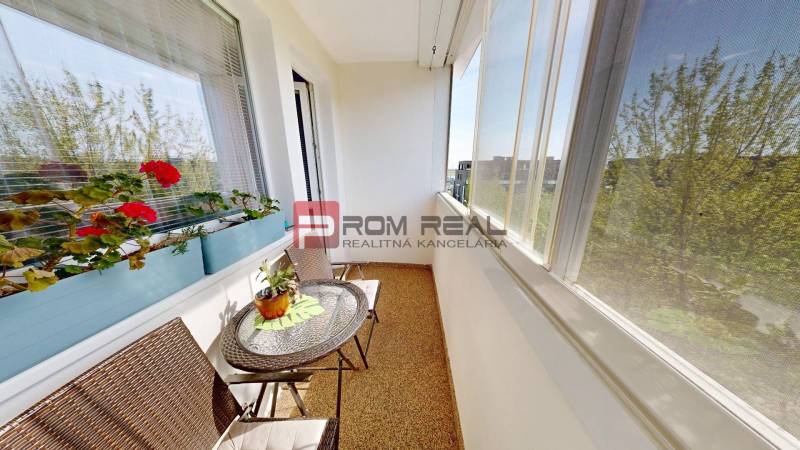 A glazed loggia with rattan furniture and flowers in a 3-room apartment.