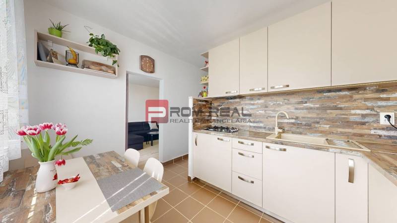 A kitchen in a 3-room apartment with a kitchenette, dining table, and flowers in a vase on the table.