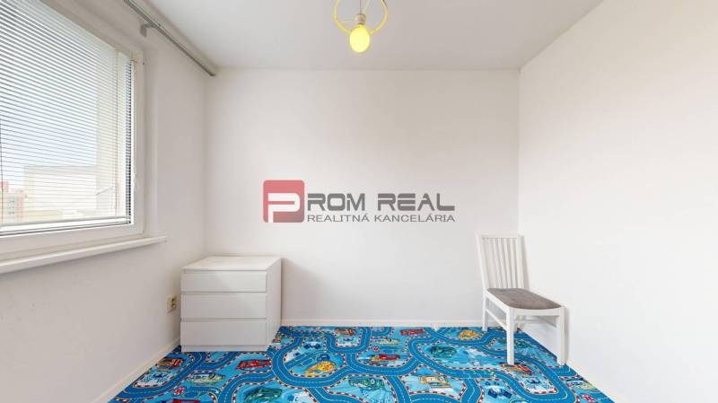 An empty room with a colorful carpet, a chair, and a dresser in a 4-room apartment.