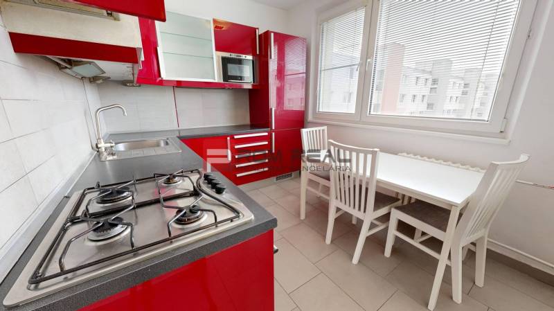 Kitchen of a 4-room apartment with red cabinets, a gas stove, and a dining table.