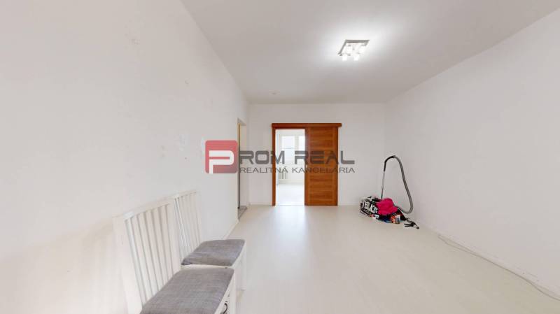 A bright room in a 4-room apartment with sliding doors and chairs. A vacuum cleaner set aside on the floor.