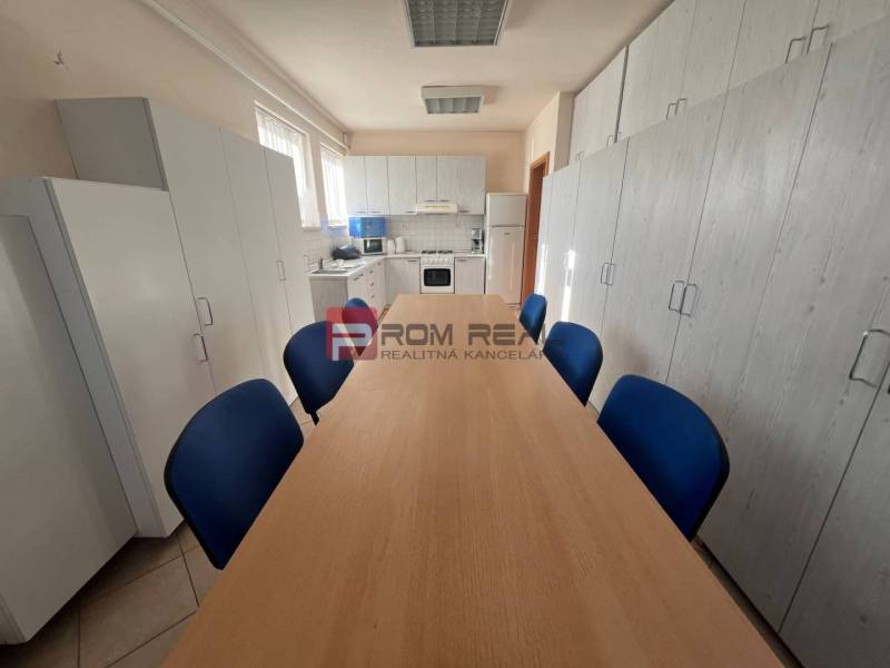 A kitchenette in the production area with a wooden table, blue chairs, and white cabinets.