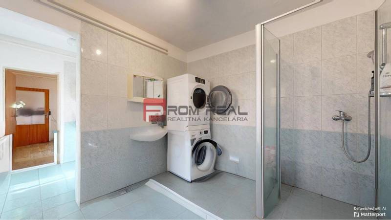 A bathroom in a family house with a washing machine, dryer, and shower stall.