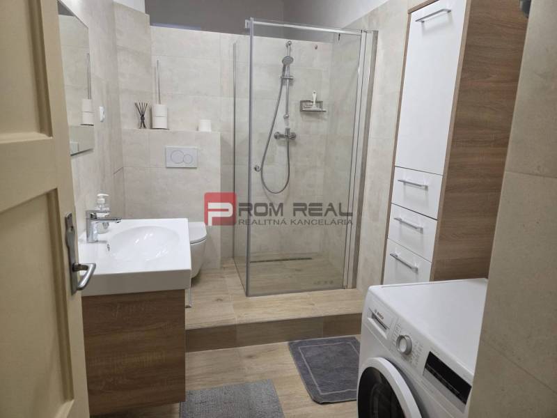 A bathroom with a shower and a washing machine in a 2-room apartment.
