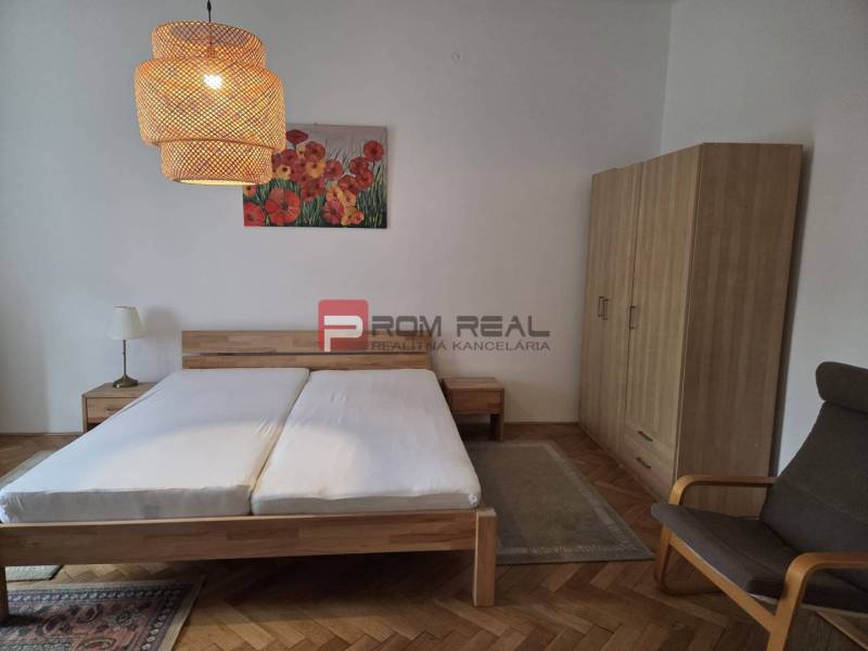 Bedroom in a 2-room apartment with wooden furniture, chandeliers, and a painting with flowers.
