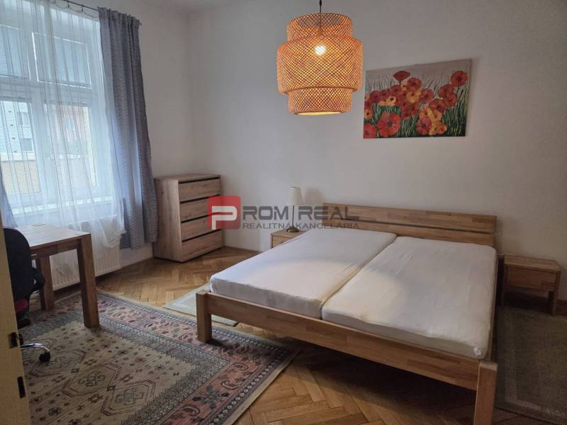 A bedroom with a wooden bed, a desk, and light decor in a 2-room apartment.