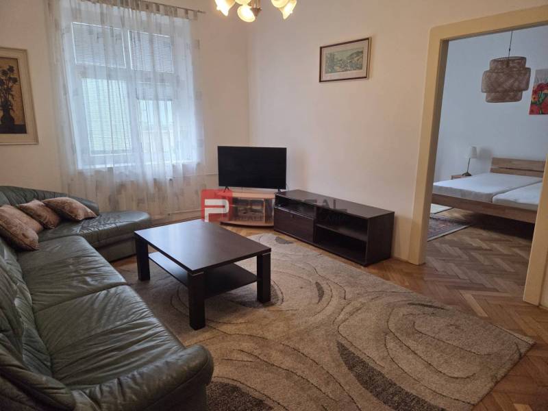 Living room in a two-room apartment, with a sofa, television, and a view into the bedroom.