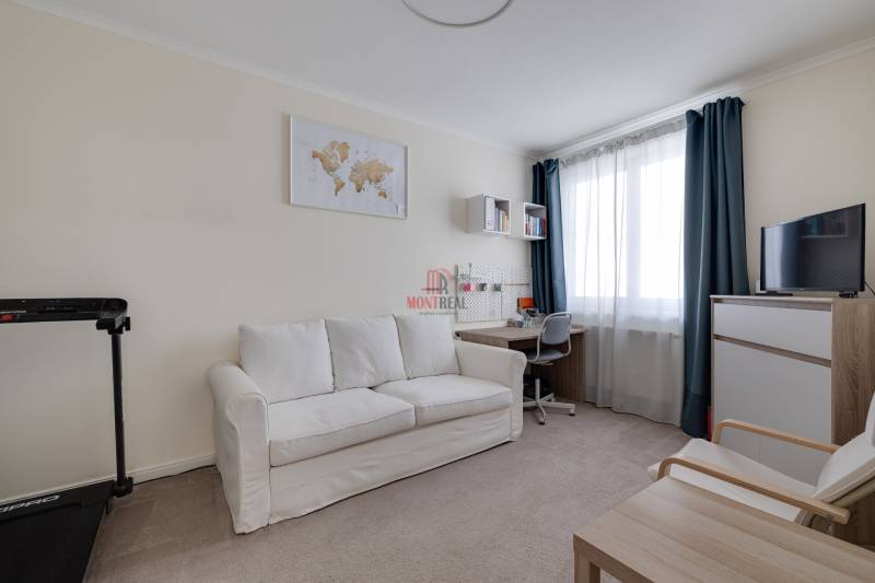 A room in a 3-room apartment with a sofa, a desk, and a television.
