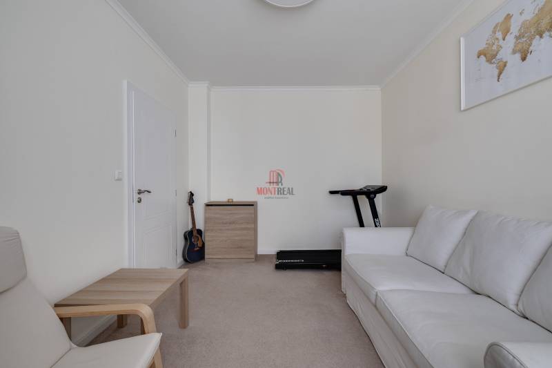 A room in a 3-room apartment with a white couch, a guitar, and a treadmill.