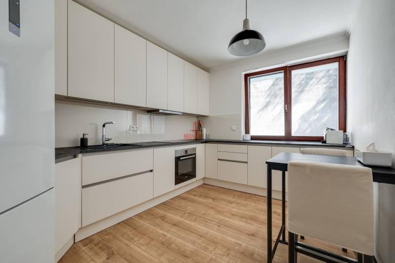 A kitchen in a 3-room apartment with wooden flooring and white cabinets.