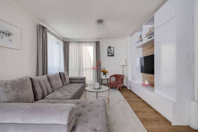 A bright living room with a large gray sofa and a TV wall in a three-room apartment.