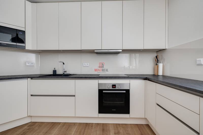 A kitchen in a 3-room apartment with white cabinets and a dark countertop.