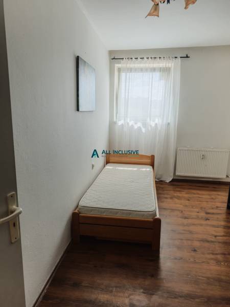 A single bed in a room with a window and a curtain in a 2-room apartment.