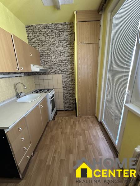 A kitchen with wooden cabinets, a stove, and a sink in a studio apartment.