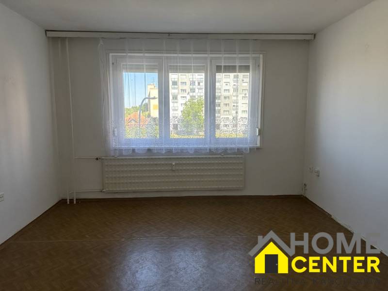 A room in a one-bedroom apartment with parquet floors, a large window, and a radiator.