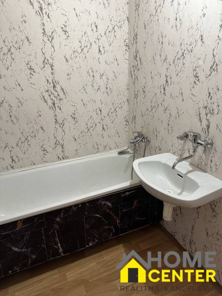 Bathroom in a studio apartment with a bathtub and a sink, marble-look walls.
