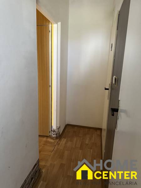 A hallway in a one-room apartment with wooden flooring, white walls, and open doors.