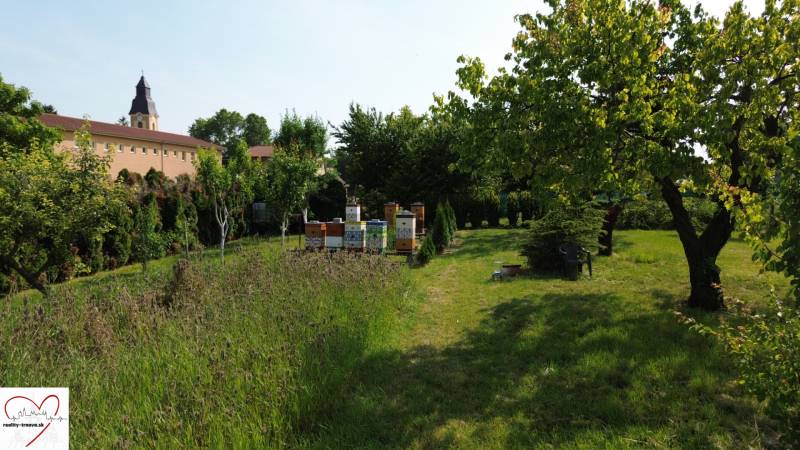 Green residential plots in Dolný Bar with beehives, surrounded by trees.