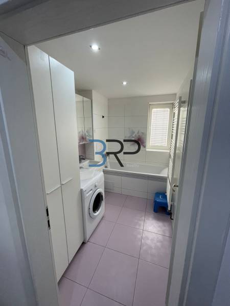 A bathroom in a 2-room apartment with a washing machine, bathtub, sink, and storage spaces.