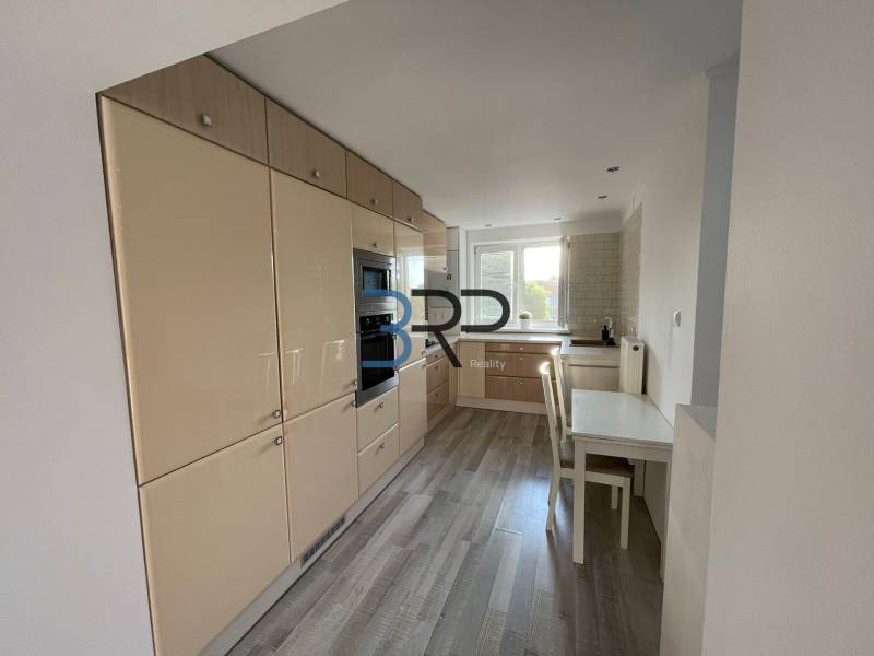 A kitchen in a 2-room apartment with white furniture and wooden flooring.
