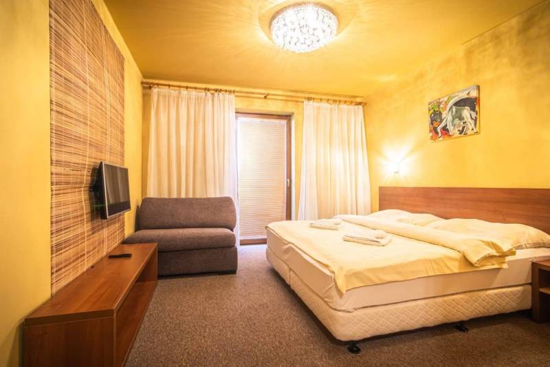 A bedroom in a holiday apartment with a double bed, a sofa, and a television.