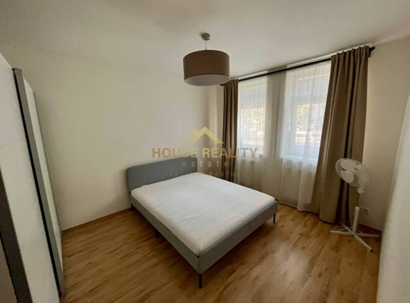 Bright bedroom with a bed and windows, 2-room apartment with wooden flooring and curtains.