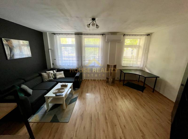 Living room with a black sofa, white table, and a desk in a two-room apartment.