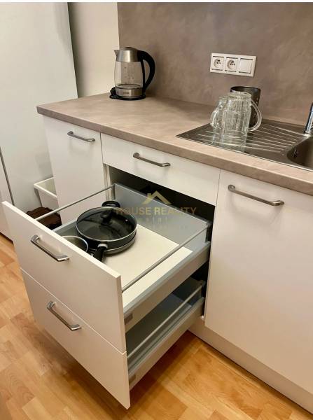 A kitchen with white cabinets, an open drawer, a sink, and an electric kettle in a two-room apartment.