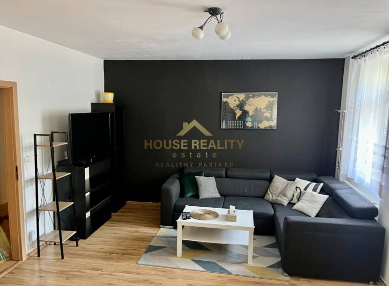 Living room in a two-room apartment with a sofa, table, and TV on a dark wall.
