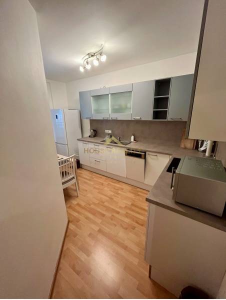 A kitchen in a 2-room apartment with wooden flooring, white furniture, and appliances.